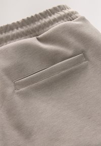 Pantaloni della tuta grigio chiaro con tessuto strutturato, vita elastica e tasca posteriore orizzontale con apertura rettangolare.