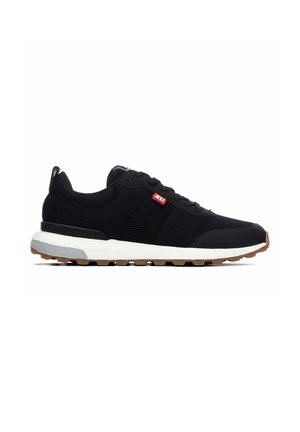 Zapatilla deportiva negra de malla con suela blanca, dibujo de goma, cordones negros y una pequeña etiqueta roja en el lateral con texto blanco "XTI".