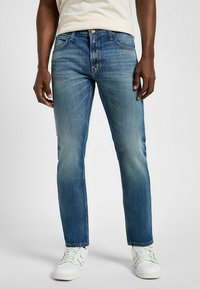 Granatowe dżinsy o prostym kroju, z wyblakłym wykończeniem, pięcioma kieszeniami i zapinane na guzik, w połączeniu z białymi trampkami.