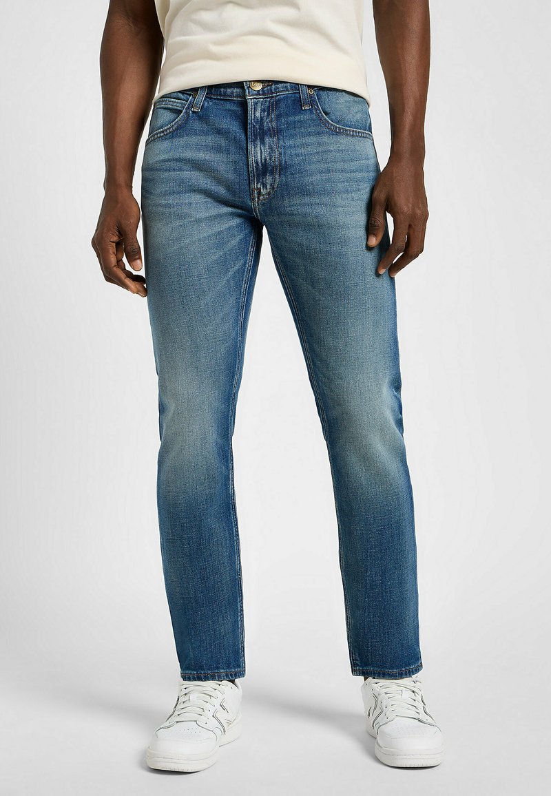 Granatowe dżinsy o prostym kroju, z wyblakłym wykończeniem, pięcioma kieszeniami i zapinane na guzik, w połączeniu z białymi trampkami.