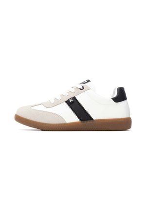 Zapatilla blanca con una punta de cuero de ante color crema, una franja negra a lo largo del costado, talón negro y una suela de goma texturizada color caramelo. Los cordones son blancos.