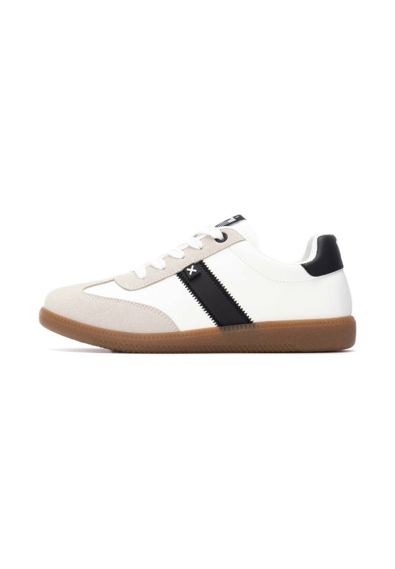 Zapatilla blanca con una punta de cuero de ante color crema, una franja negra a lo largo del costado, talón negro y una suela de goma texturizada color caramelo. Los cordones son blancos.