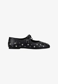 Zapato plano de cuero negro con tachuelas redondas de plata y un pequeño lazo en la parte superior, visto de lado sobre un fondo blanco.
