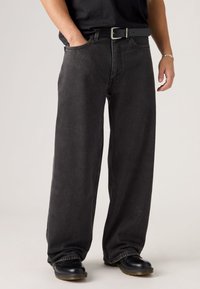 Black, wide-leg jeans made of denim, featuring a classic five-pocket design, high waist, and visible stitching details, worn with a belt.