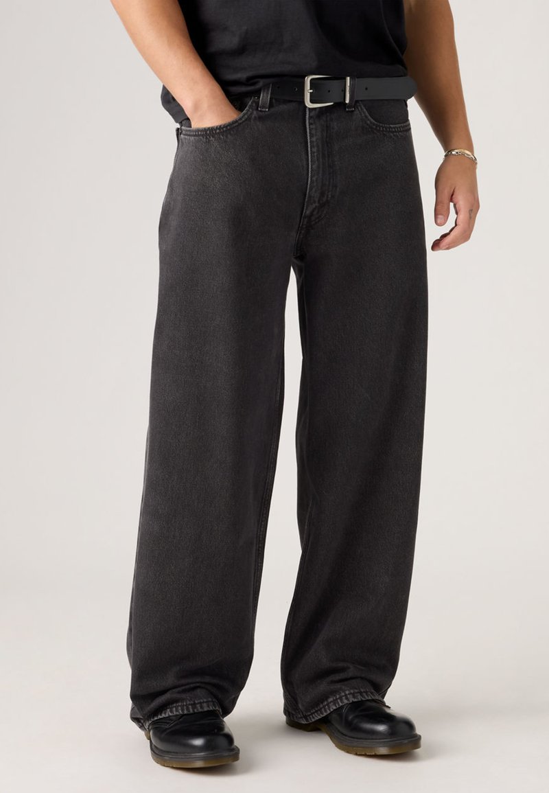 Black, wide-leg jeans made of denim, featuring a classic five-pocket design, high waist, and visible stitching details, worn with a belt.