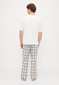 Vit bomullt-shirt och rutig pyjamasbyxor i grått, beige och blått. Pyjamasbyxorna har en löst sittande passform och en rak benstil.