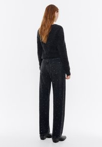 Mustad denim püksid, millel on lahtine lõige ja mitmevärvilised nupud. Modell kannab tumedat, karvast sviitrit ja kontsaga saapaid.