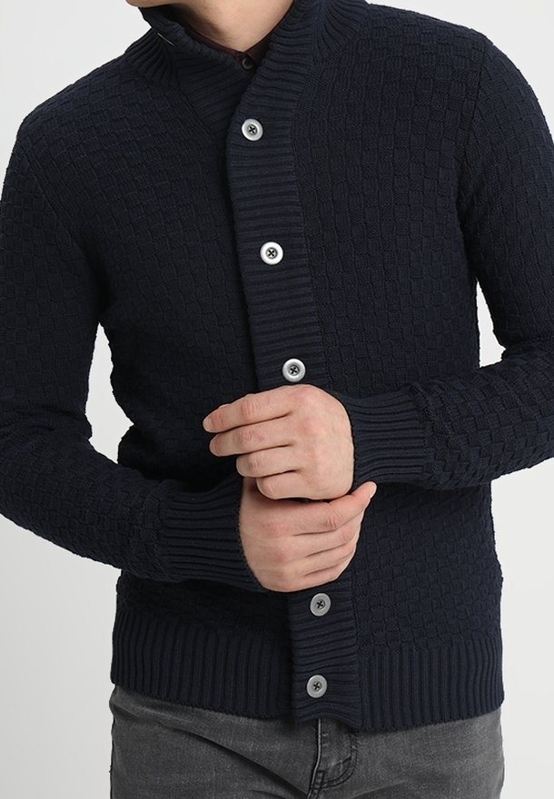 Marinblå stickad cardigan med ett strukturerat mönster, hög krage och fem stora knappar. Ribbad ärmslut och nederkant. Åtsittande design.