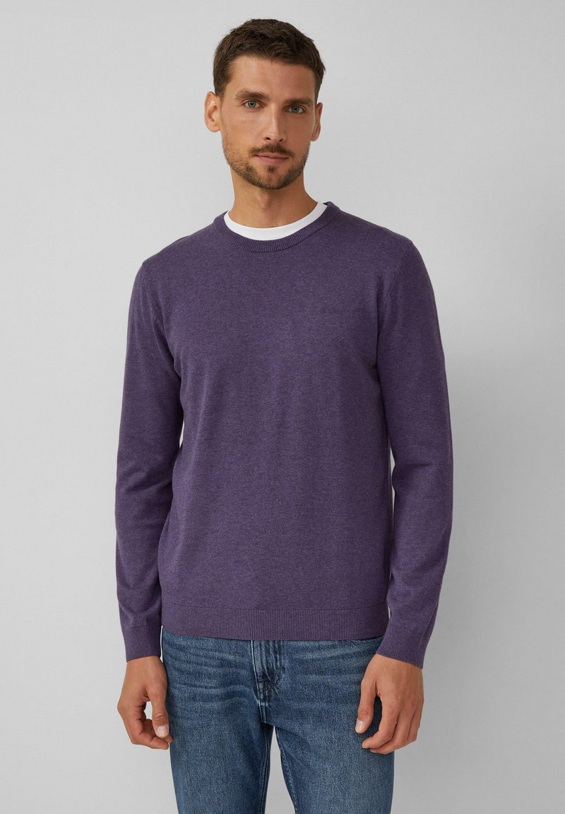 Lila Rundhalsausschnitt-Pullover aus Strickstoff mit langen Ärmeln. Verfügt über einen gerippten Saum und Bündchen. Getragen über einem weißen Hemd mit Kragen.