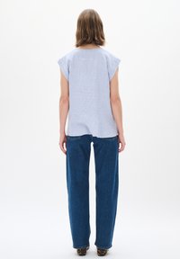 Tops s modrými a bielymi pruhmi s krátkymi rukávmi, v kombinácii s voľnými tmavomodrými džínsami. Hladká tkanina, neformálny dizajn, viditeľné detaily šitia.