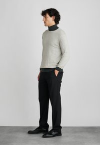 Lysegrå strikkegenser med mørkegrønne aksenter, kombinert med svarte bukser. Antrekket har rund hals og lange ermer.