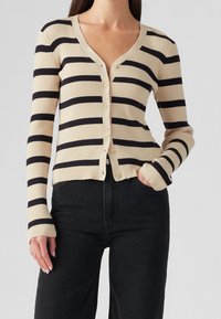 Beżowo-granatowy prążkowany kardigan w paski z dekoltem w serek i guzikami z przodu. Posiada długie rękawy i krótki, przycięty dół.