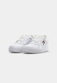 Baskets blanches en cuir lisse avec un design à lacets, des languettes rembourrées et un logo avec des accents rouge, blanc et bleu sur le côté.