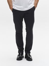 Sötétkék, texturált anyagból készült, testhez simuló, oldalanként zsebes nadrág, fekete, fényes cipővel és fehér pólóval viselve.