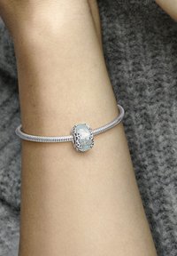 Strieborný hadí náramok so strednou akvamarínovou sklovou guľou uzavretou v dekoratívnej kovovej sponke, prezentujúci hladký povrch.