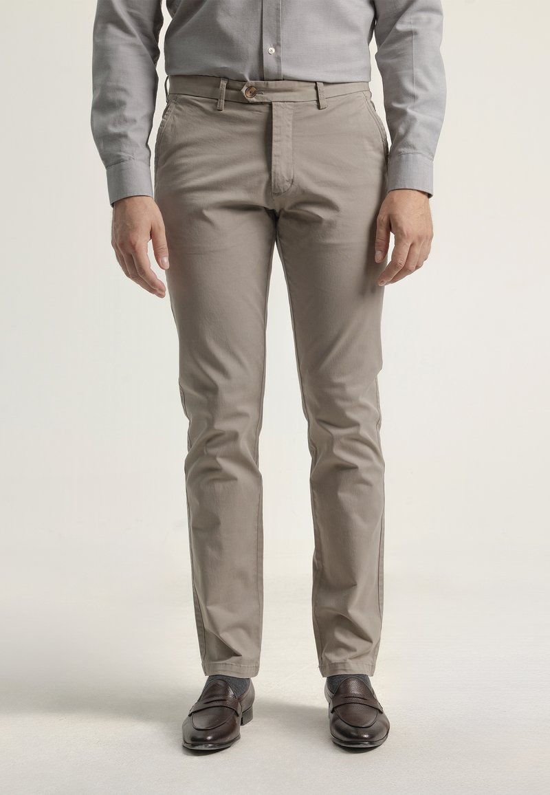 Chinos beige claros hechos de una mezcla de algodón, con un corte recto en la parte delantera, bolsillos laterales y cierre de botón. Llevados con mocasines marrón oscuro.