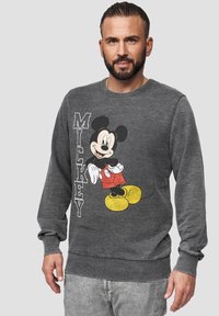 Šedá mikina s dlouhými rukávy a žebrovanými manžetami, na které je grafika Mickey Mouse v červených šortkách a žlutých botách, s textem "MICKEY".