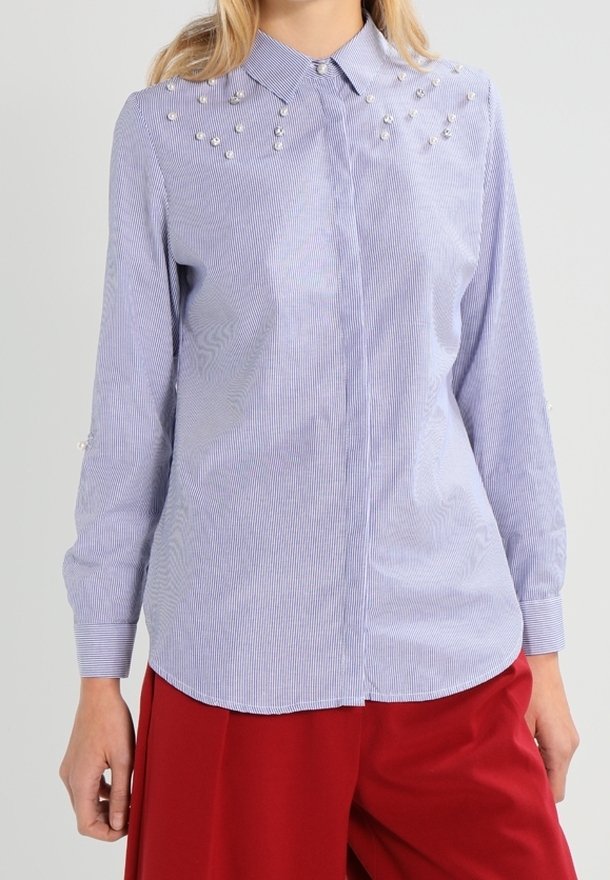 Striped button-up shirt in blue and white cotton, featuring pearl accents on shoulders and cuffs, long sleeves, and a rounded hem.