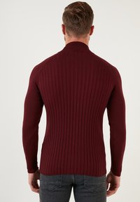 Burgunderfarbener gerippter Pullover mit hohem Kragen und tailliertem Schnitt, der ein strukturiertes Muster und lange Ärmel präsentiert.
