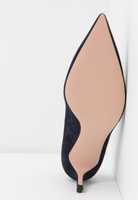 Chaussure à talon haut en daim bleu marine avec un bout pointu, dotée d'une semelle beige et d'un talon fin noir pour un design élégant.