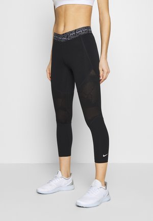 Czarne legginsy sportowe z teksturowanym siateczkowym wzorem, z markowym pasem w talii, zestawione z białymi sneakersami.