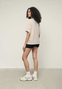 Světle béžové oversized tričko, krátké černé žebrované šortky, bílé sportovní ponožky a krémové tenisky. Model stojí zády k fotoaparátu.