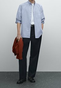 Jasnoniebieska koszula w paski z guzikami, biała koszulka, ciemne spodnie, trzymając czerwony sweter, ubrane czarne buty. Prosty, czysty design.