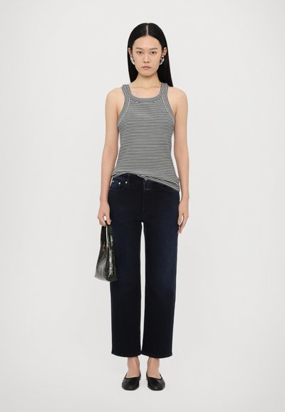 Stribet ærmeløs top, mørke jeans, sorte flade sko og en lille grøn håndtaske i krokodilleskindsstruktur. Enkel design, tætsiddende top, lige ben jeans.