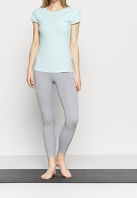 Camiseta ajustada de color azul claro con mangas cortas, combinada con leggings de color gris claro. Ambas prendas están hechas de un material suave y elástico.