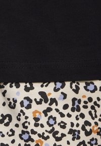 Black cotton top featuring a leopard print pattern in black, orange, and light blue on a cream background, with a visible hem and texture contrast.