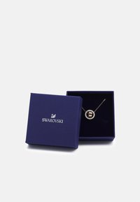 Swarovski halskæde i en bl�å boks. Har en rund vedhæng med en brun sten omgivet af klare krystaller på en fin kæde.