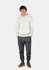 Weißer Hoodie mit Kängurutasche, graue schmal geschnittene Hose und grüne Sneaker. Der Hoodie hat ein einfaches Design mit einem Logo-Detail auf der Vorderseite.