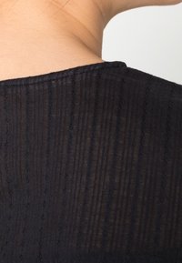Tessuto nero testurizzato con strisce verticali e cuciture sottili. Lo scollo ha una finitura liscia, creando un design pulito e minimalista.