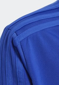 Modré sportovní tričko s texturovanou tkaninou, které má tři vodorovné pruhy na rameni. Lehce a prodyšné provedení.