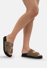 Bruna mockaskinnsandaletter med två breda remmar med spännen, en formad svart gummisula och en öppen tå-design. Texturerad yta.