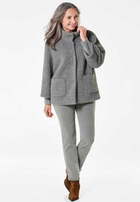 Grau strukturierter Strickpullover mit einem Stehkragen, ausgestattet mit zwei vorderen Taschen; kombiniert mit grauen Hosen und braunen Ankle-Boots.