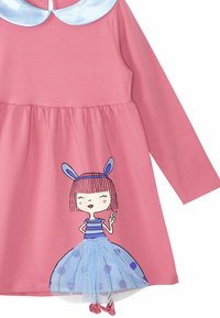 Vaaleanpunainen pitkähiha dressi, jossa on vaaleansininen kaulus. Mallissa on kuvio tytöstä, joka on pukeutunut raidalliseen paitaan ja tüllihameeseen, jossa on pilkkuja.