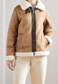 Brown faux suede jacket with a white shearling collar and cuffs. Features a front zipper and side pockets. Textured surface.