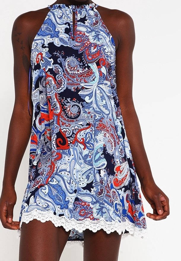 Robe sans manches avec un motif paisley bleu, rouge et blanc, décolleté halter, détail en forme de trou de serrure, et bord inférieur en dentelle blanche.