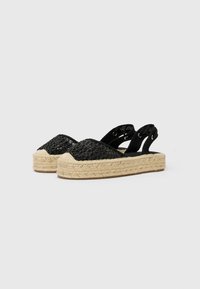 Sandali espadrilles neri intrecciati con suola in juta, caratterizzati da un design a punta chiusa e cinturini alla caviglia regolabili con occhielli in metallo.