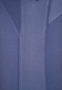 Gros plan sur un tissu bleu extensible avec un panneau central texturé et des panneaux latéraux lisses cousus ensemble avec des coutures visibles.