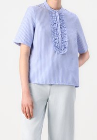 Haut à manches courtes rayé bleu clair avec un plastron froncé à l'avant, un col rond et des boutons ; associé à un pantalon en denim clair.