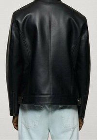 Czarna skórzana kurtka motocyklowa o dopasowanym kroju, podkreślająca gładką teksturę, pionowe szwy i metalowe elementy przy talii.