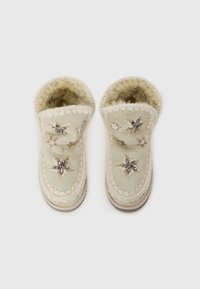 Beige slippers lavet af blødt materiale, med dekorativ broderi og perleudsmykninger. Rundet form med en fluffy indvendig foring.