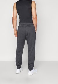 Gray sweatpants with a relaxed fit, elastic waistband, and side pockets, paired with white athletic shoes and a sleeveless black top.