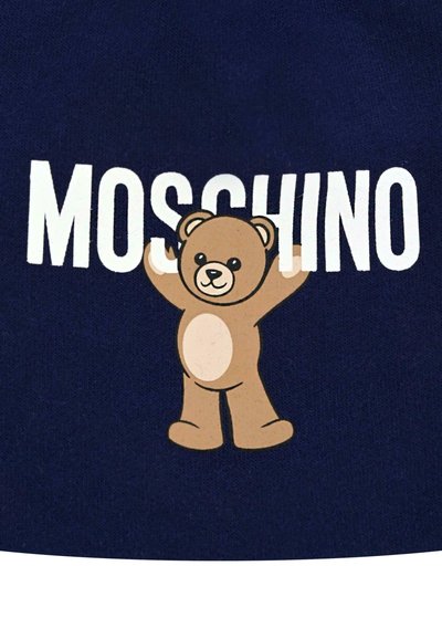Il tessuto blu navy presenta un orso dei cartoni animati di colore beige con la pancia crema, le braccia alzate, accanto al testo "MOSCHINO" in grandi lettere bianche.