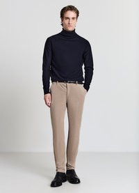 Marineblauer Rollkragenpullover mit strukturiertem Muster, kombiniert mit hellbeigen Hosen und schwarzen Leder-Stiefeletten. Schlichte, moderne Silhouette.