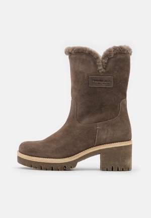 Stivale marrone in suede fino a metà polpaccio con interno in pelliccia, tacco spesso, suola carrarmato e etichetta "Panama Jack" sul lato.