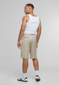 Beige shorts gemaakt van lichtgewicht stof, met een normale pasvorm en zijzakken. Gecombineerd met een wit tanktop en zwarte sneakers.