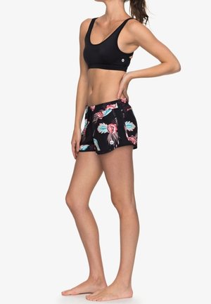 Sujetador deportivo negro combinado con pantalones cortos de estampado floral que presentan toques de turquesa y rosa, confeccionados en tela ligera.